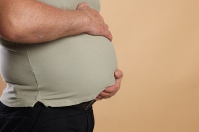 Photo of Overweight man in tight t-shirt on beige background, closeup. Space for text