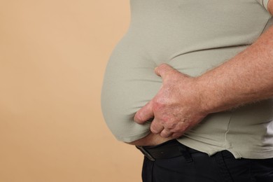 Photo of Overweight man in tight t-shirt on beige background, closeup. Space for text