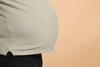 Photo of Overweight man in tight t-shirt on beige background, closeup. Space for text