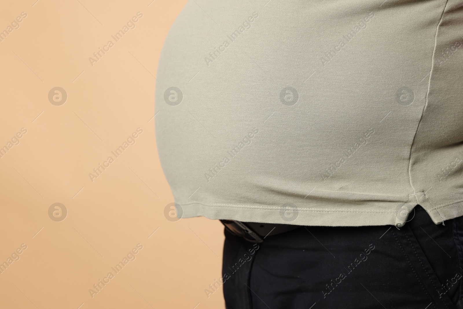 Photo of Overweight man in tight t-shirt on beige background, closeup. Space for text