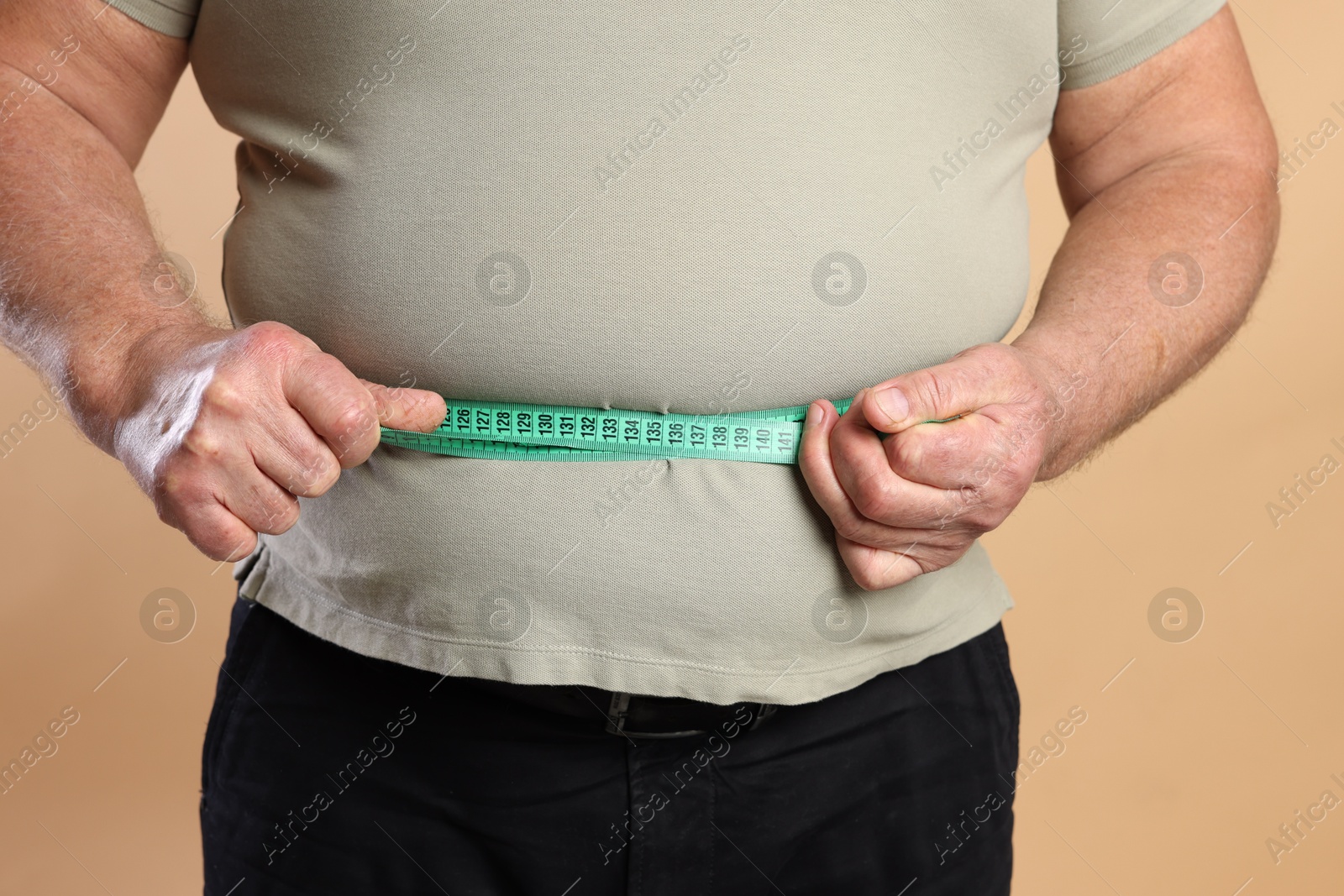 Photo of Overweight man measuring his belly with tape on beige background, closeup