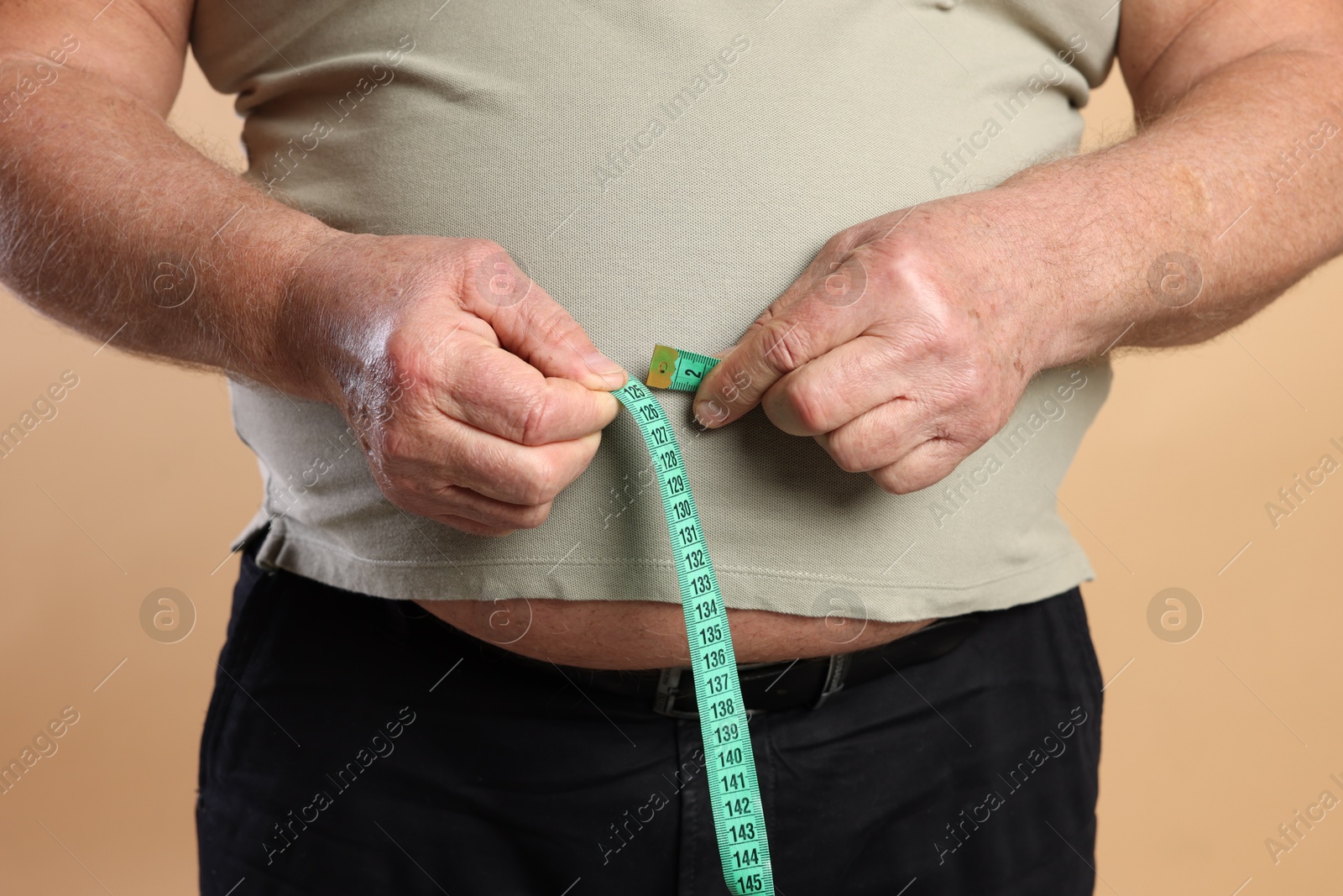 Photo of Overweight man measuring his belly with tape on beige background, closeup