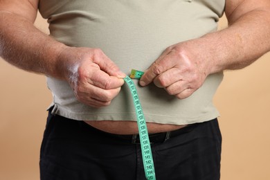 Photo of Overweight man measuring his belly with tape on beige background, closeup