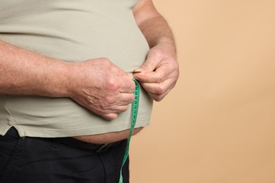 Photo of Overweight man measuring his belly with tape on beige background, closeup. Space for text