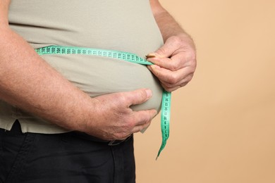 Photo of Overweight man measuring his belly with tape on beige background, closeup. Space for text