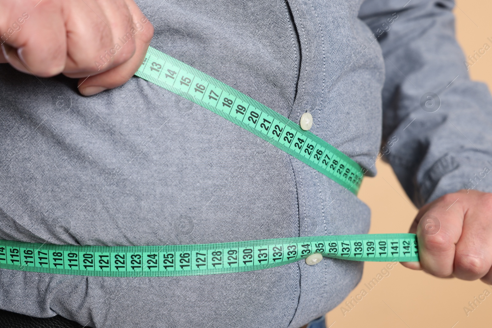 Photo of Overweight man measuring his belly with tape on beige background, closeup