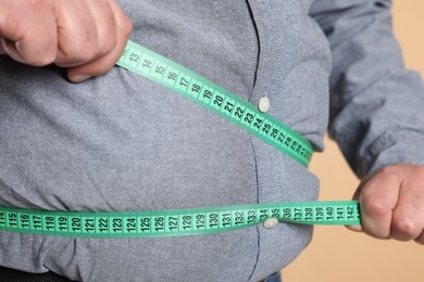 Photo of Overweight man measuring his belly with tape on beige background, closeup