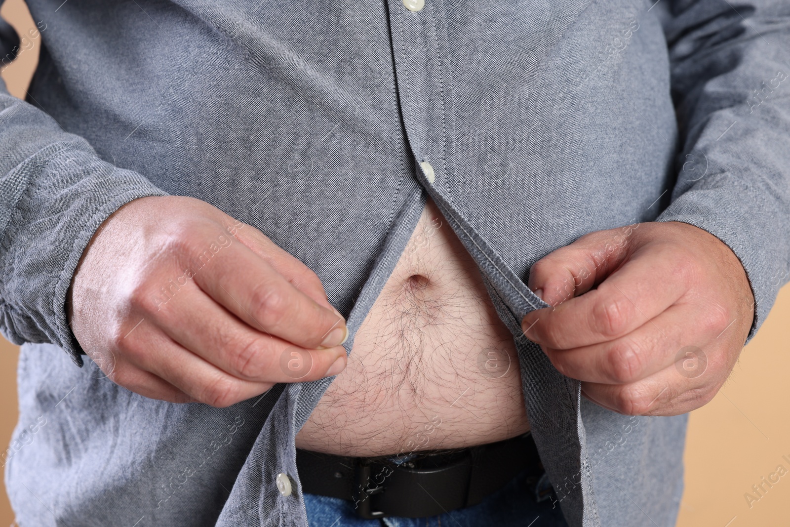 Photo of Overweight man trying to button up tight shirt on beige background, closeup