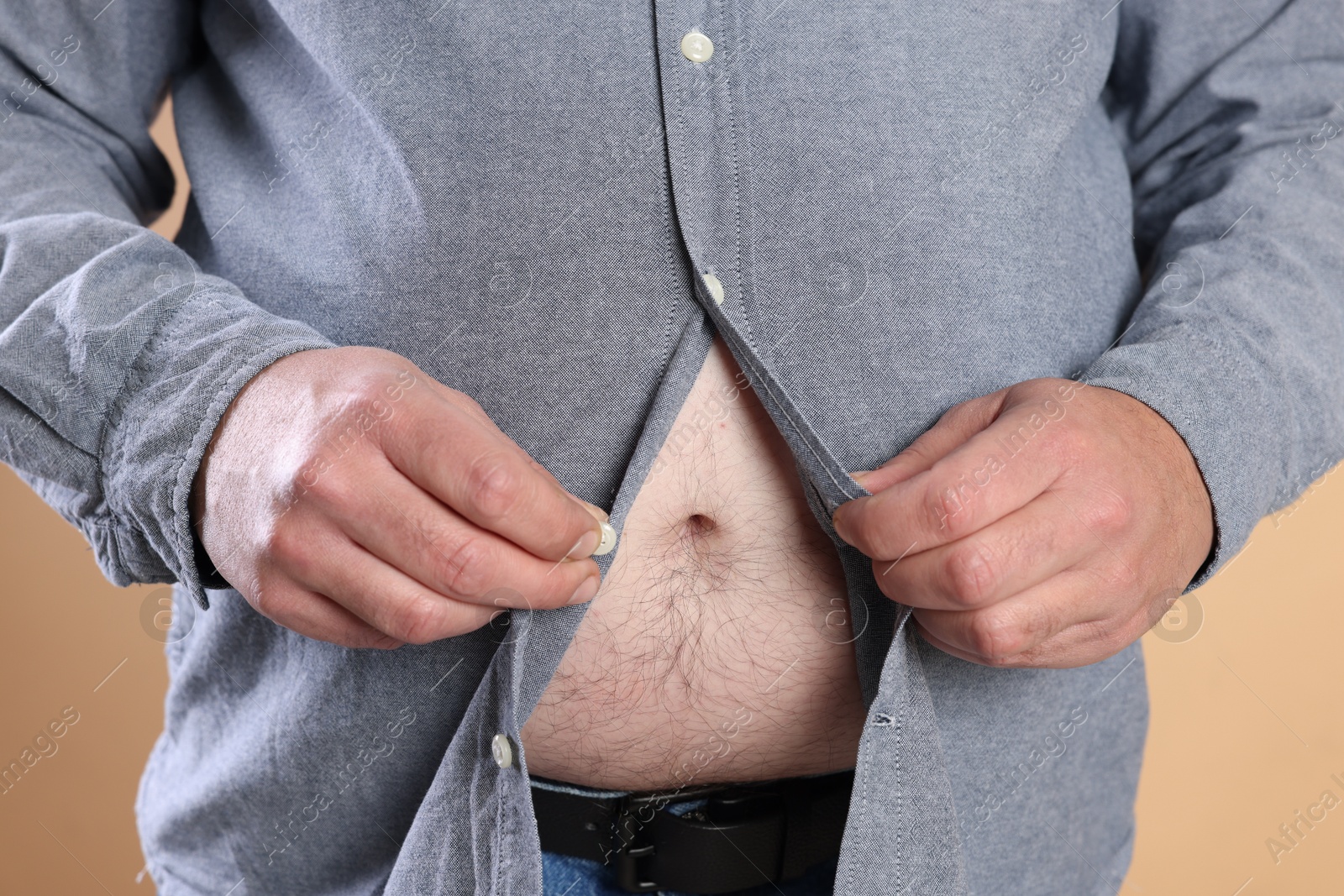 Photo of Overweight man trying to button up tight shirt on beige background, closeup