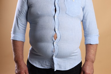 Photo of Overweight man in tight shirt on beige background, closeup