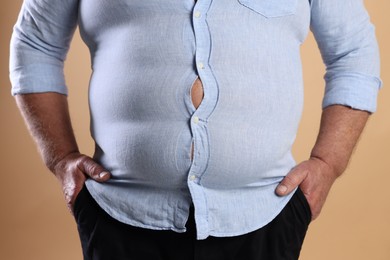 Photo of Overweight man in tight shirt on beige background, closeup