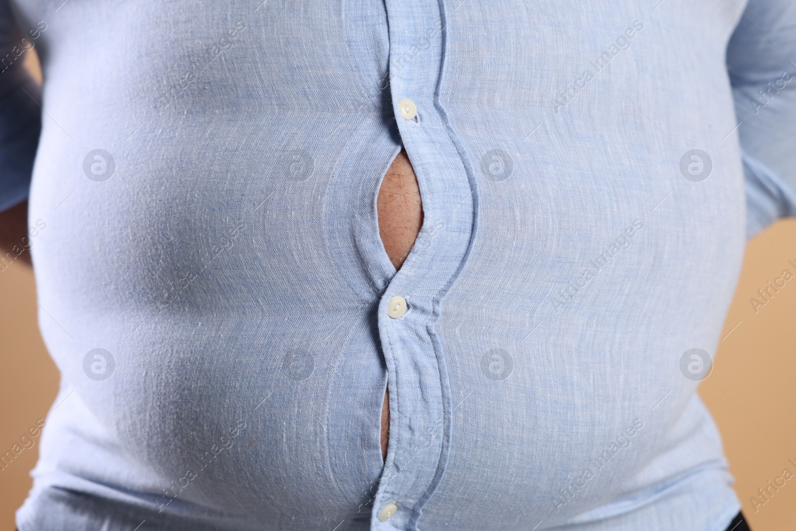 Photo of Overweight man in tight shirt on beige background, closeup