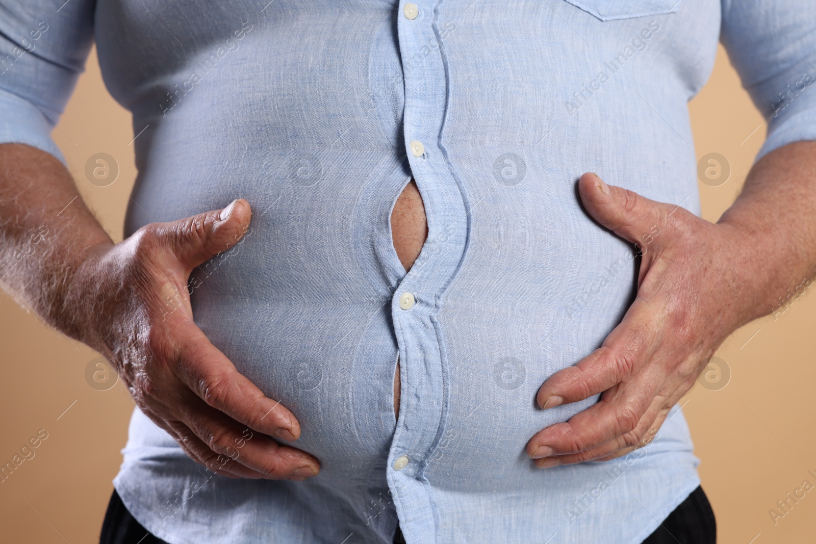 Photo of Overweight man in tight shirt on beige background, closeup