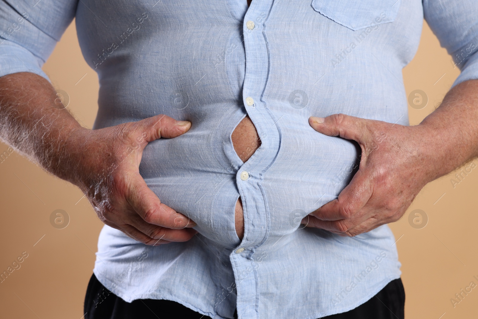 Photo of Overweight man in tight shirt on beige background, closeup