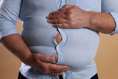 Photo of Overweight man in tight shirt on beige background, closeup