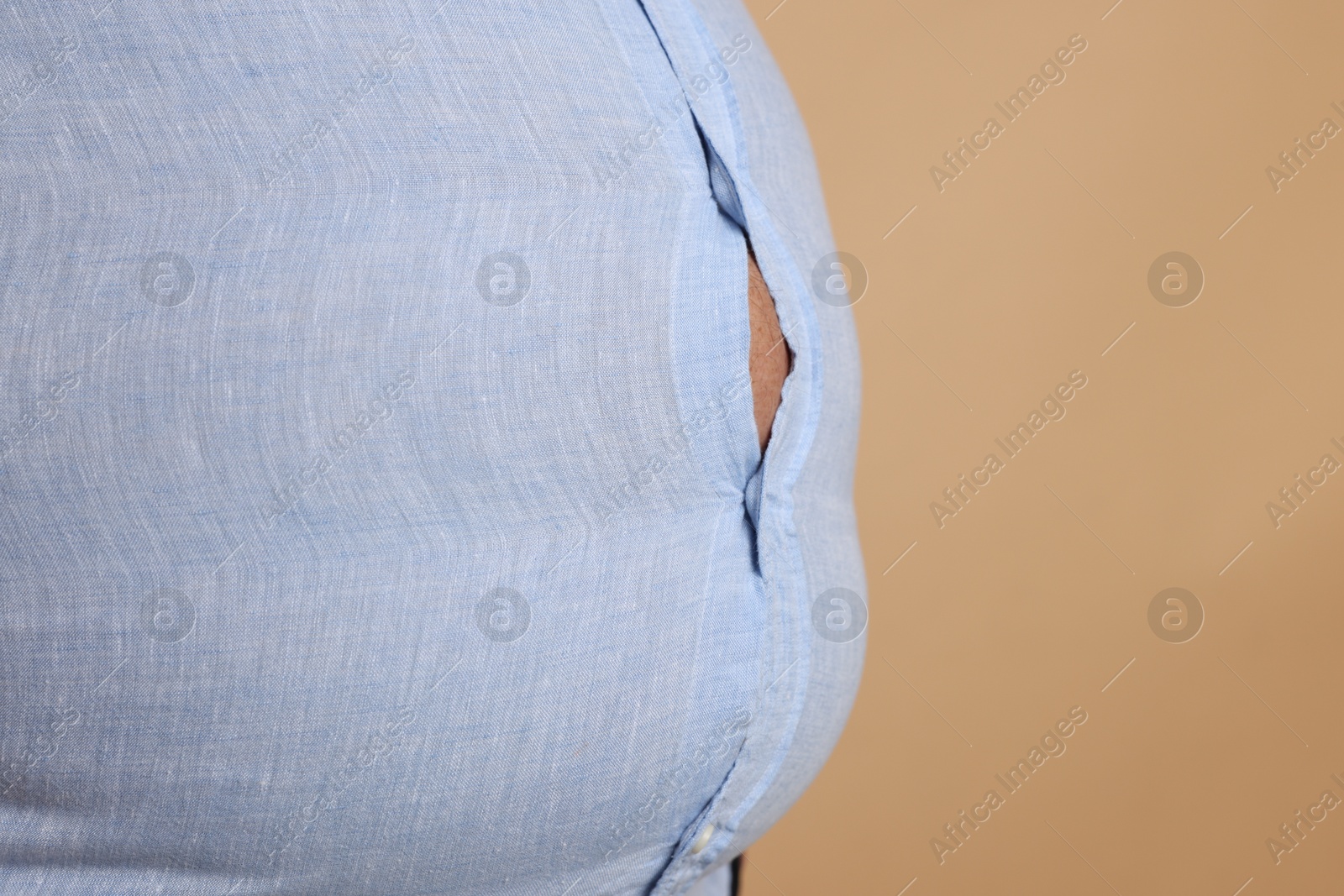 Photo of Overweight man in tight shirt on beige background, closeup. Space for text