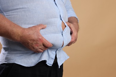 Photo of Overweight man in tight shirt on beige background, closeup. Space for text