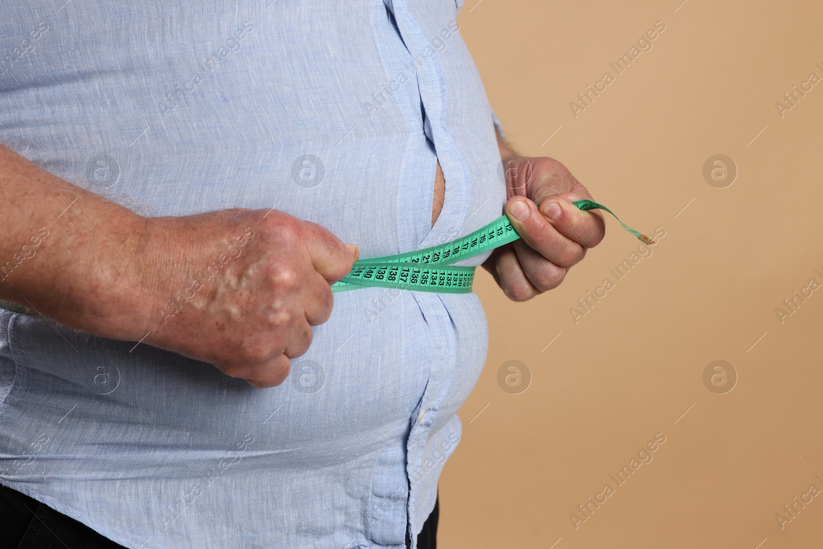 Photo of Overweight man measuring his belly with tape on beige background, closeup. Space for text