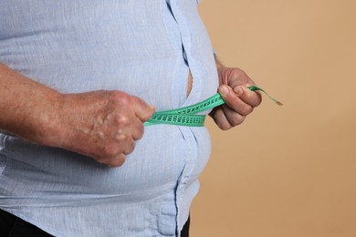 Photo of Overweight man measuring his belly with tape on beige background, closeup. Space for text