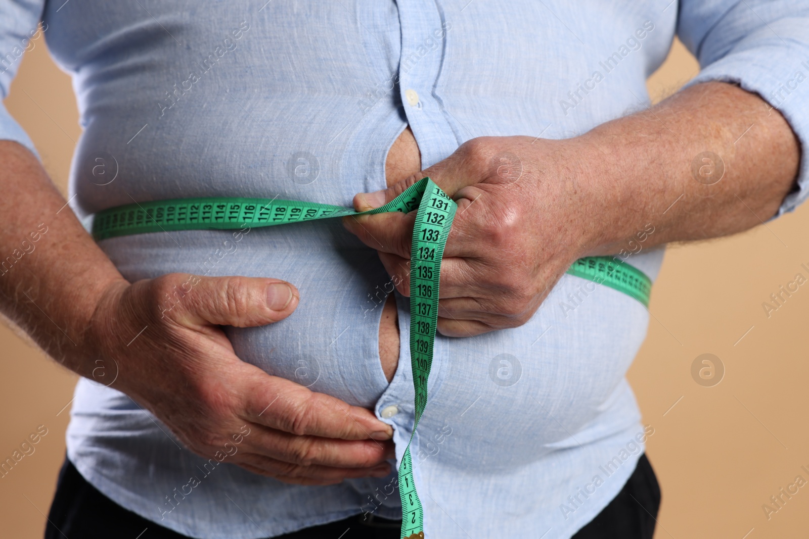 Photo of Overweight man measuring his belly with tape on beige background, closeup