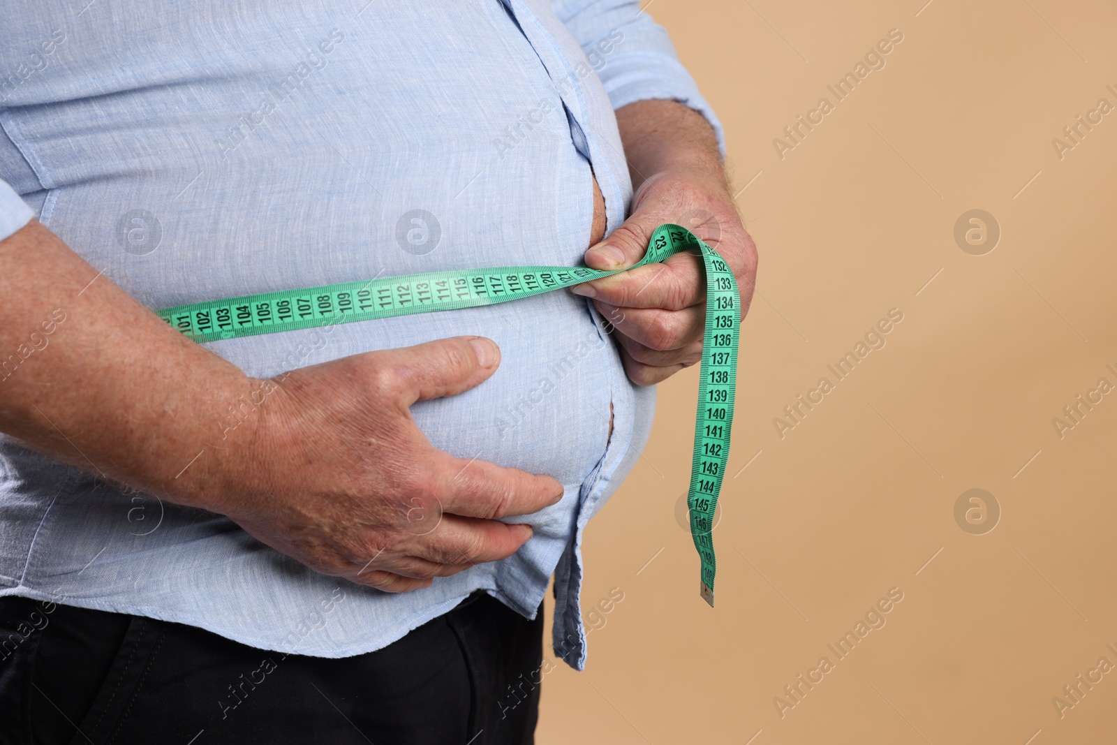 Photo of Overweight man measuring his belly with tape on beige background, closeup. Space for text