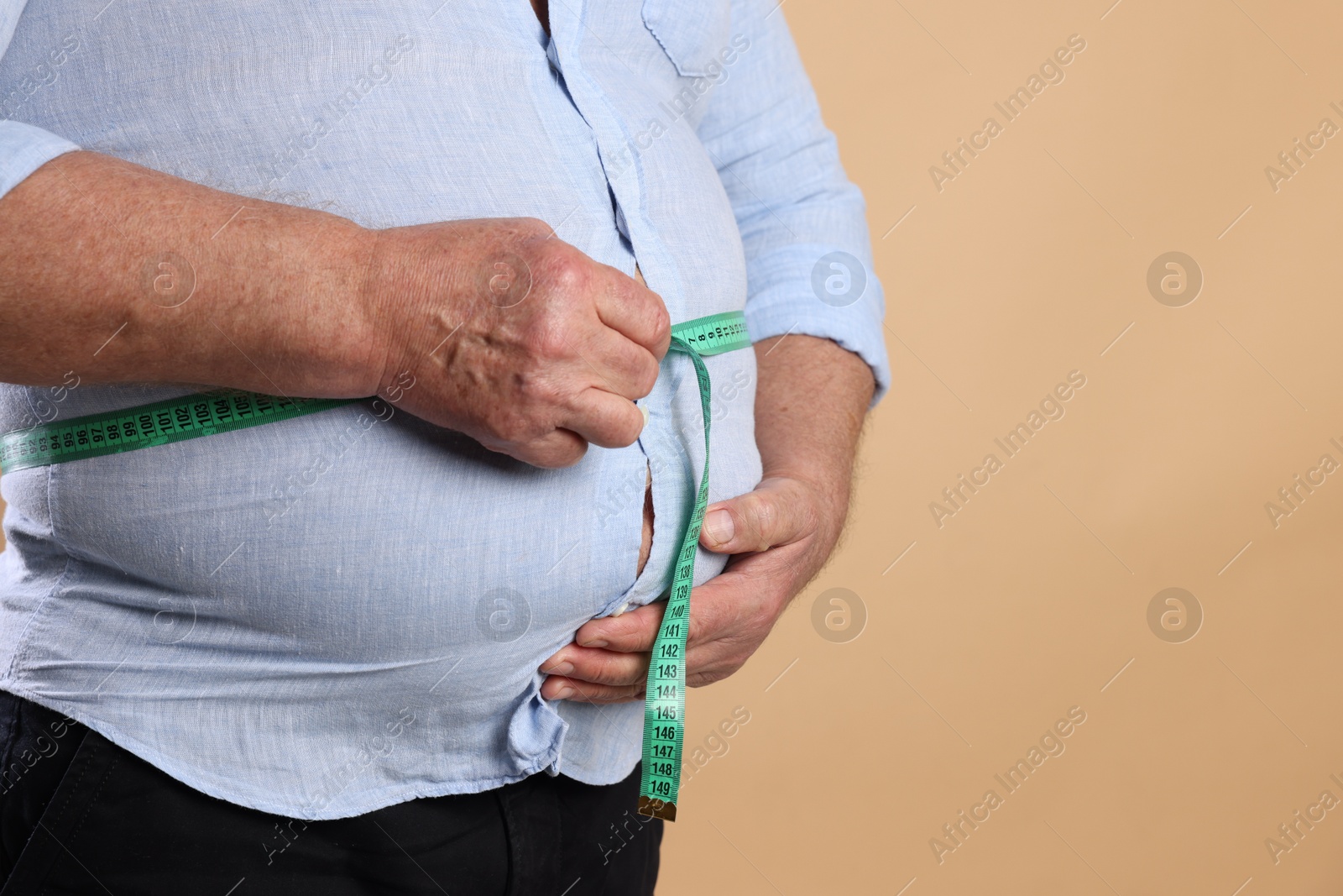 Photo of Overweight man measuring his belly with tape on beige background, closeup. Space for text