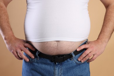 Photo of Overweight man in tight t-shirt on beige background, closeup