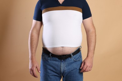 Photo of Overweight man in tight t-shirt on beige background, closeup