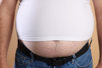 Photo of Overweight man in tight t-shirt on beige background, closeup