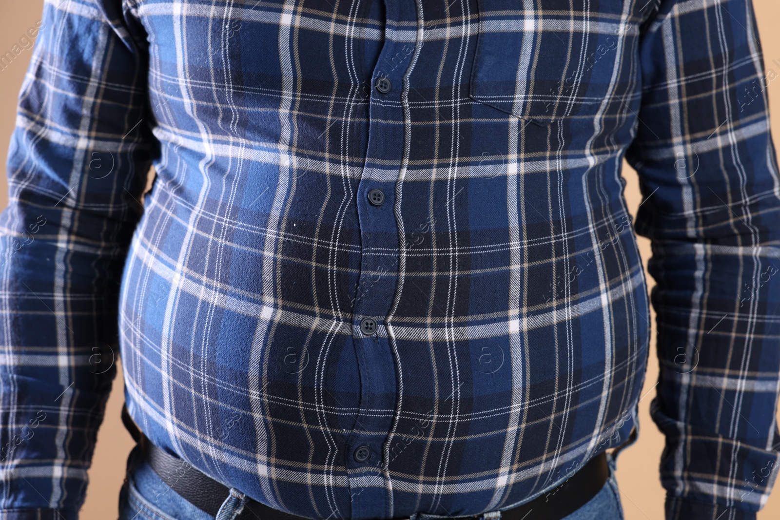 Photo of Overweight man in tight shirt on beige background, closeup