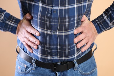 Photo of Overweight man in tight shirt on beige background, closeup