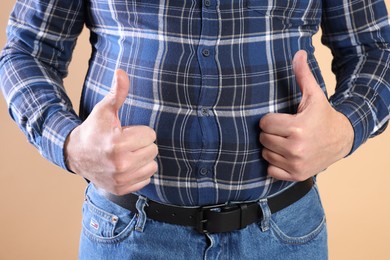 Photo of Overweight man in tight shirt showing thumbs up on beige background, closeup