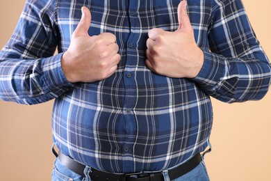 Photo of Overweight man in tight shirt showing thumbs up on beige background, closeup