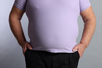 Photo of Overweight man in tight t-shirt on grey background, closeup