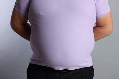 Photo of Overweight man in tight t-shirt on grey background, closeup