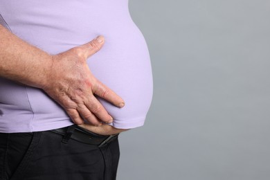 Photo of Overweight man in tight t-shirt on grey background, closeup. Space for text