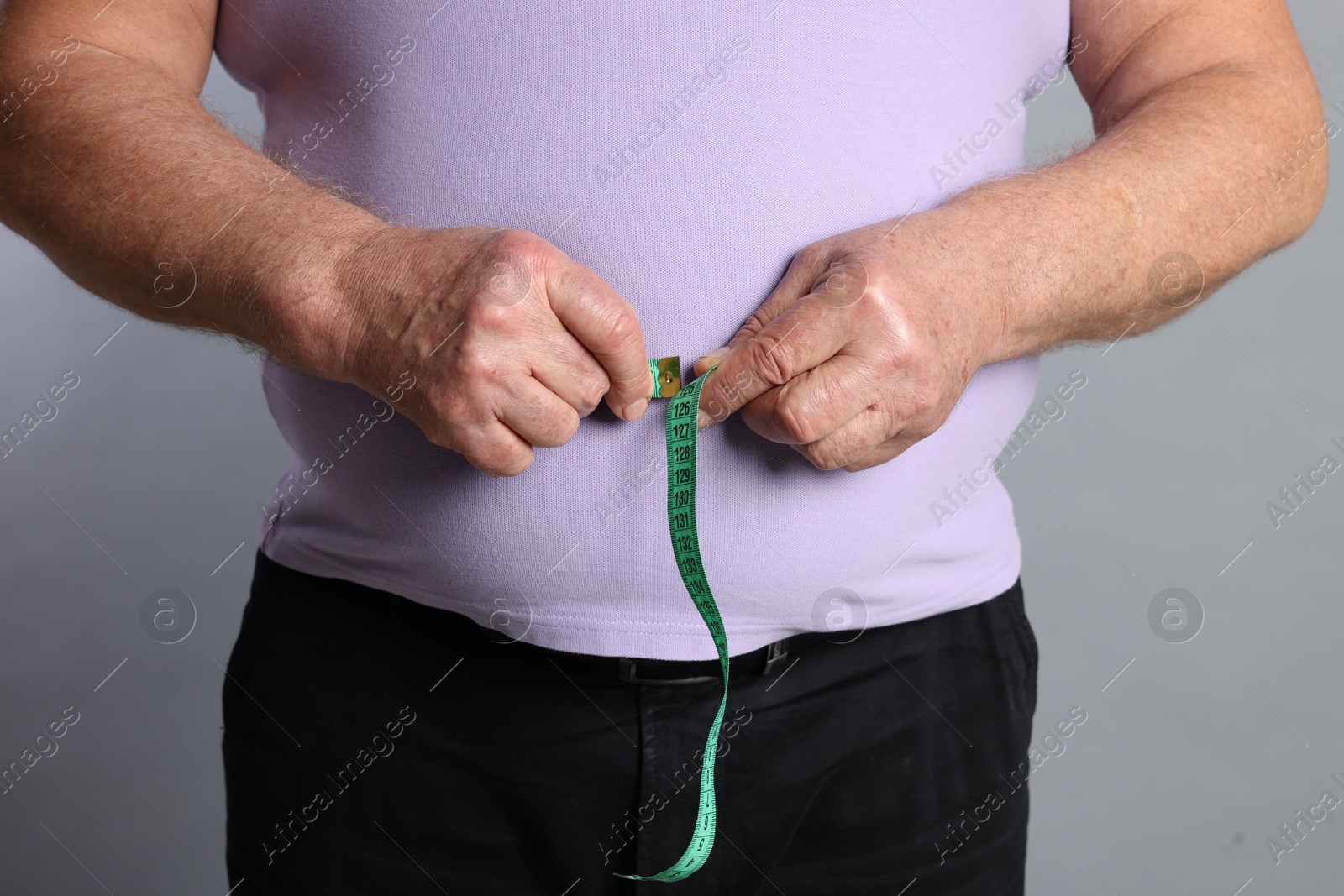 Photo of Overweight man measuring his belly with tape on grey background, closeup