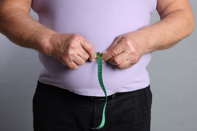 Photo of Overweight man measuring his belly with tape on grey background, closeup