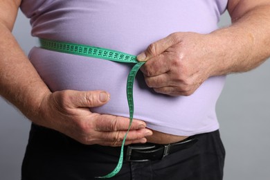 Photo of Overweight man measuring his belly with tape on grey background, closeup