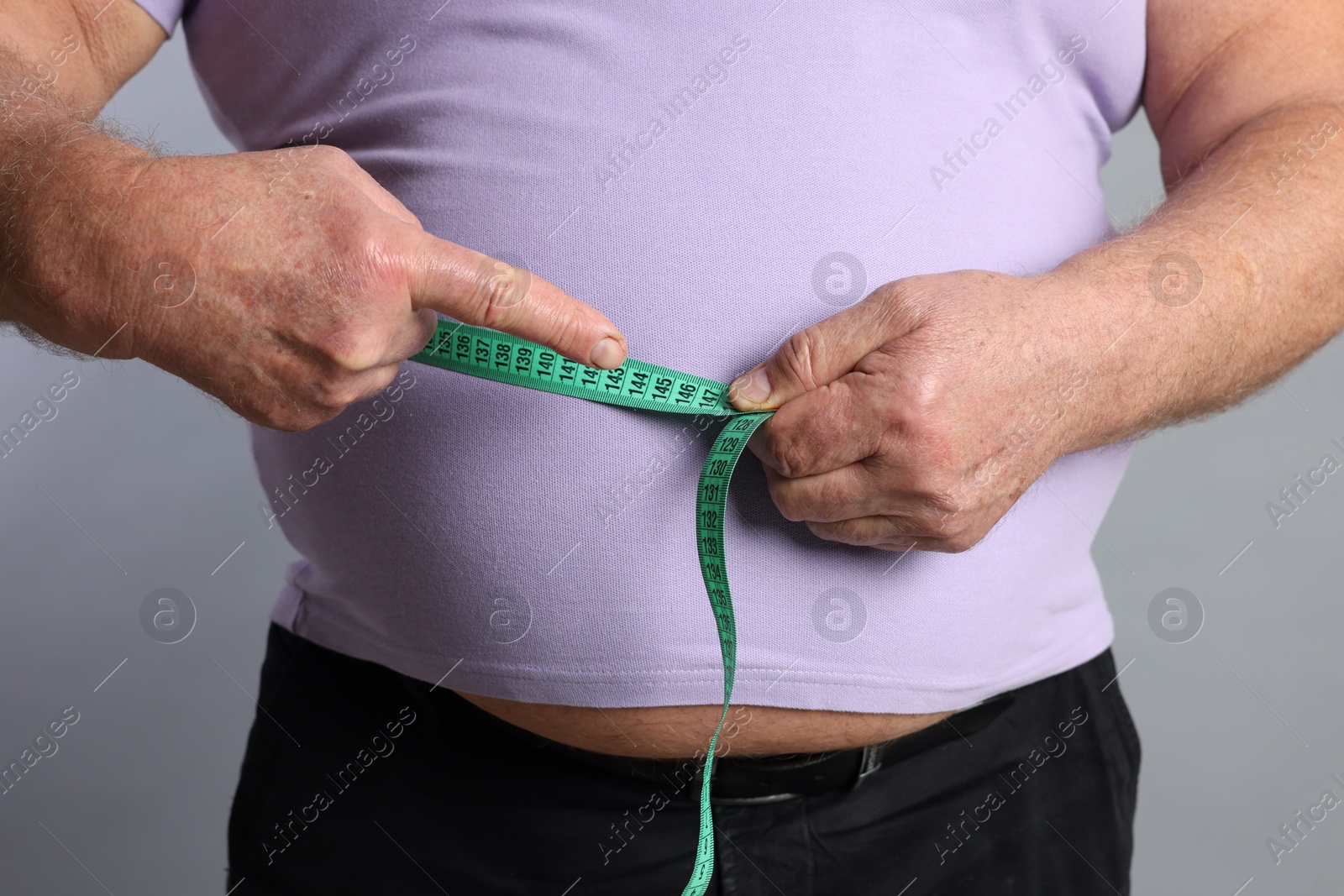 Photo of Overweight man measuring his belly with tape on grey background, closeup