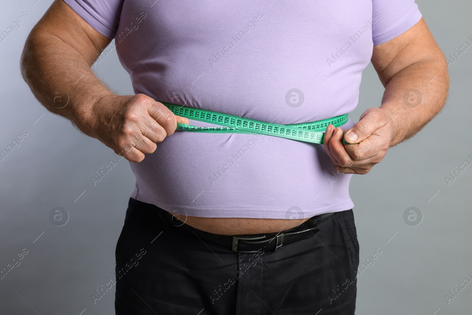 Photo of Overweight man measuring his belly with tape on grey background, closeup