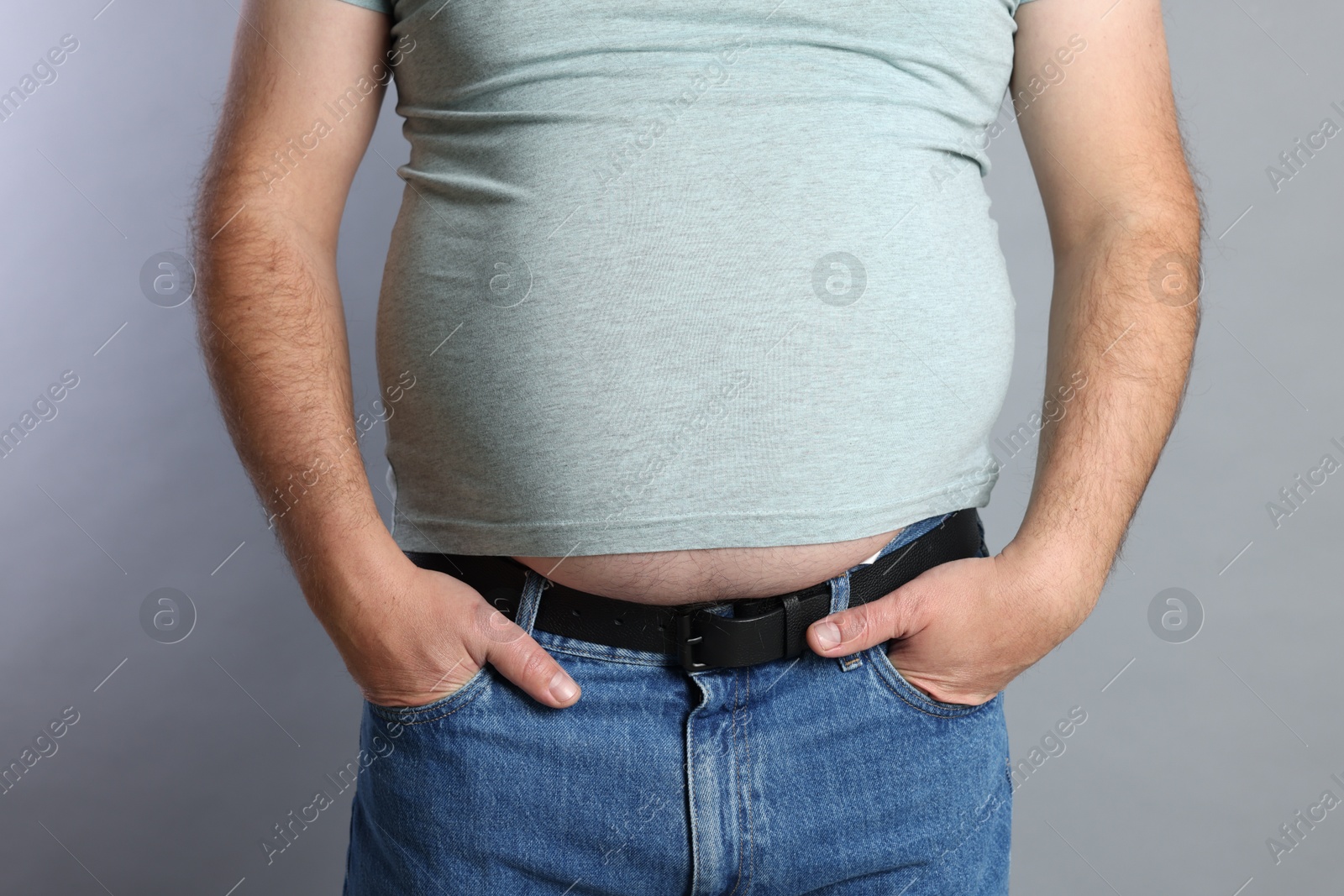 Photo of Overweight man in tight t-shirt on grey background, closeup