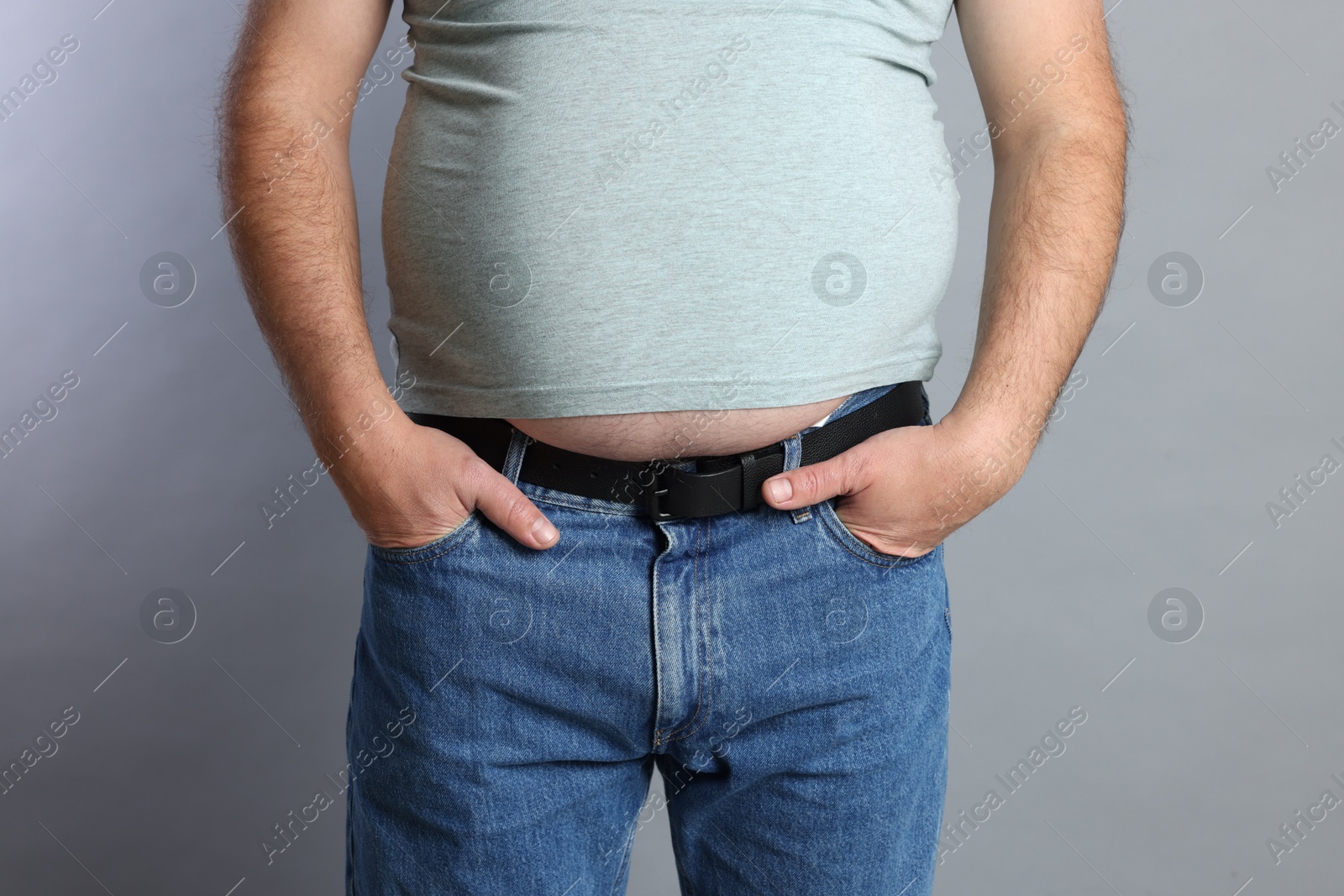 Photo of Overweight man in tight t-shirt on grey background, closeup