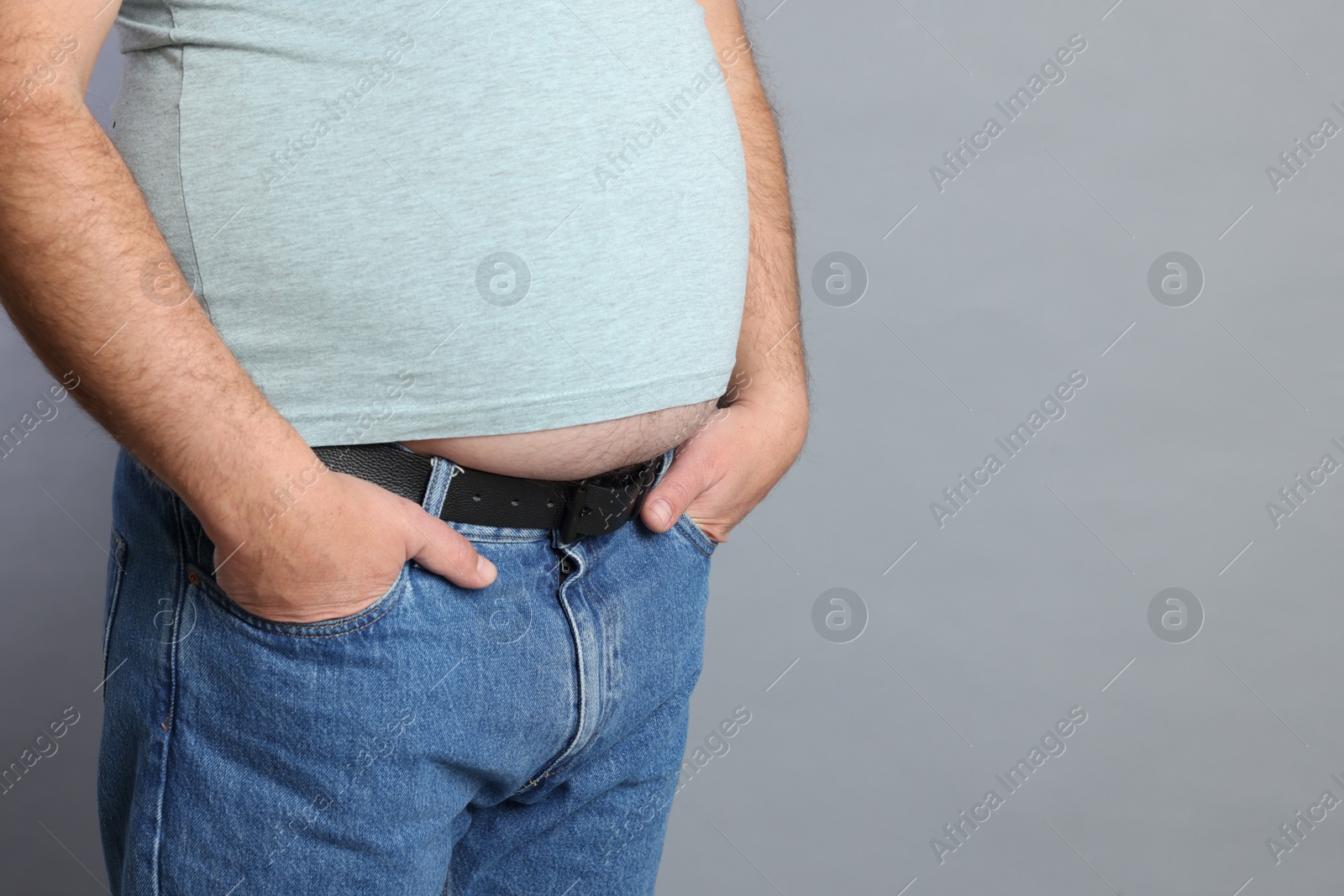 Photo of Overweight man in tight t-shirt on grey background, closeup. Space for text