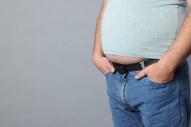 Photo of Overweight man in tight t-shirt on grey background, closeup. Space for text