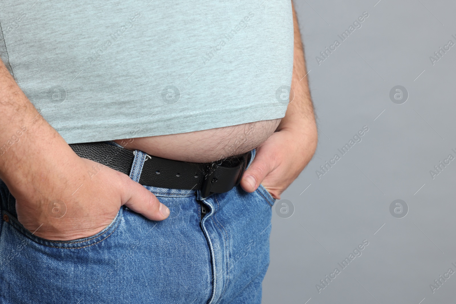 Photo of Overweight man in tight t-shirt on grey background, closeup. Space for text