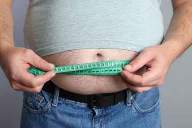 Photo of Overweight man measuring his belly with tape on grey background, closeup