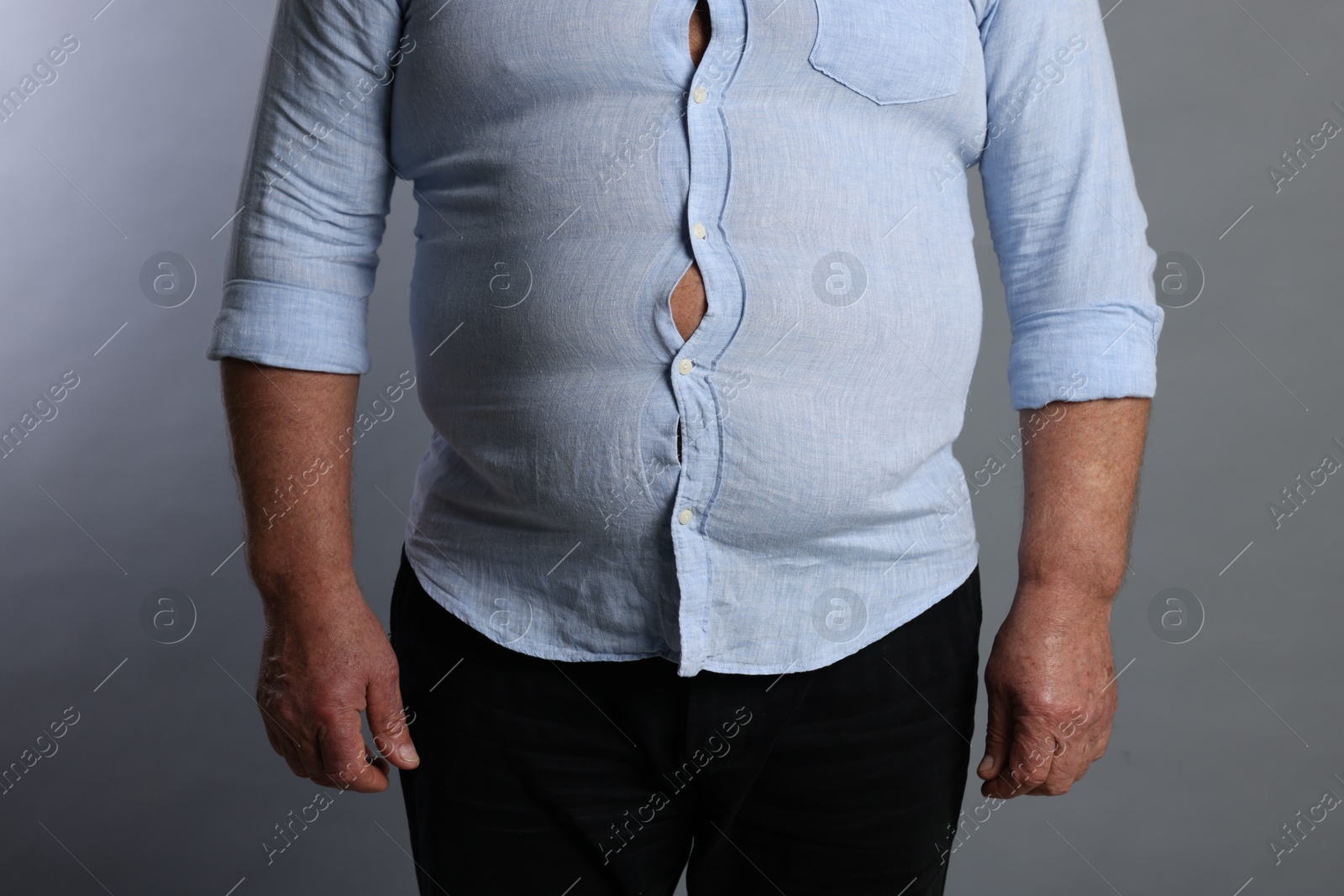 Photo of Overweight man in tight shirt on grey background, closeup