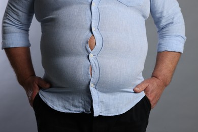 Photo of Overweight man in tight shirt on grey background, closeup