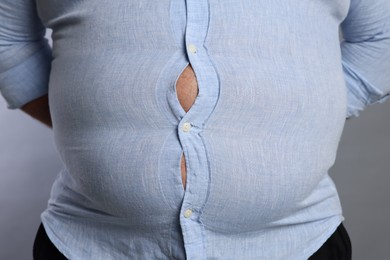 Photo of Overweight man in tight shirt on grey background, closeup